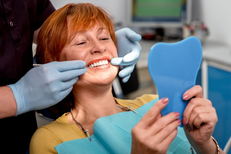 A woman admiring her dental implants in a hand mirror